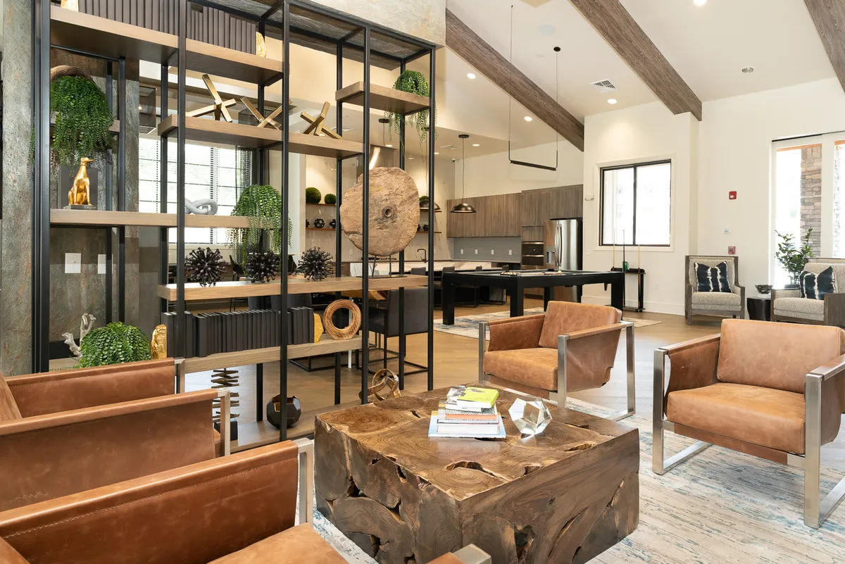 An inviting dining and living area with a wooden coffee table, metal chairs, open shelving with decor, and a glimpse of the kitchen in the background. The layout encourages both socializing and solo relaxation, and the coordinated décor ties the space together.