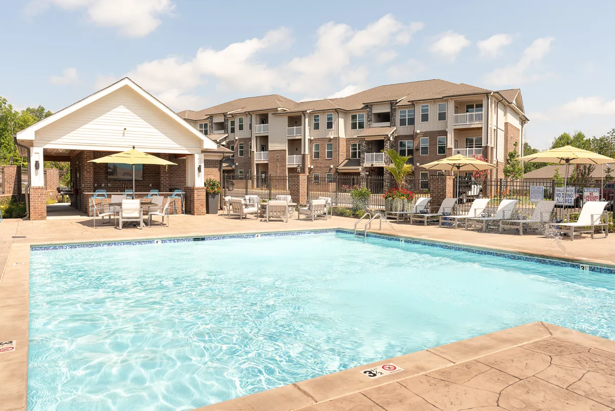 A vibrant outdoor pool area with inviting lounge seating, a pavilion, umbrellas for shade, and the backdrop of landscaped greenery. The scene exudes an atmosphere of leisure and social possibilities, perfect for relaxation after a productive day.