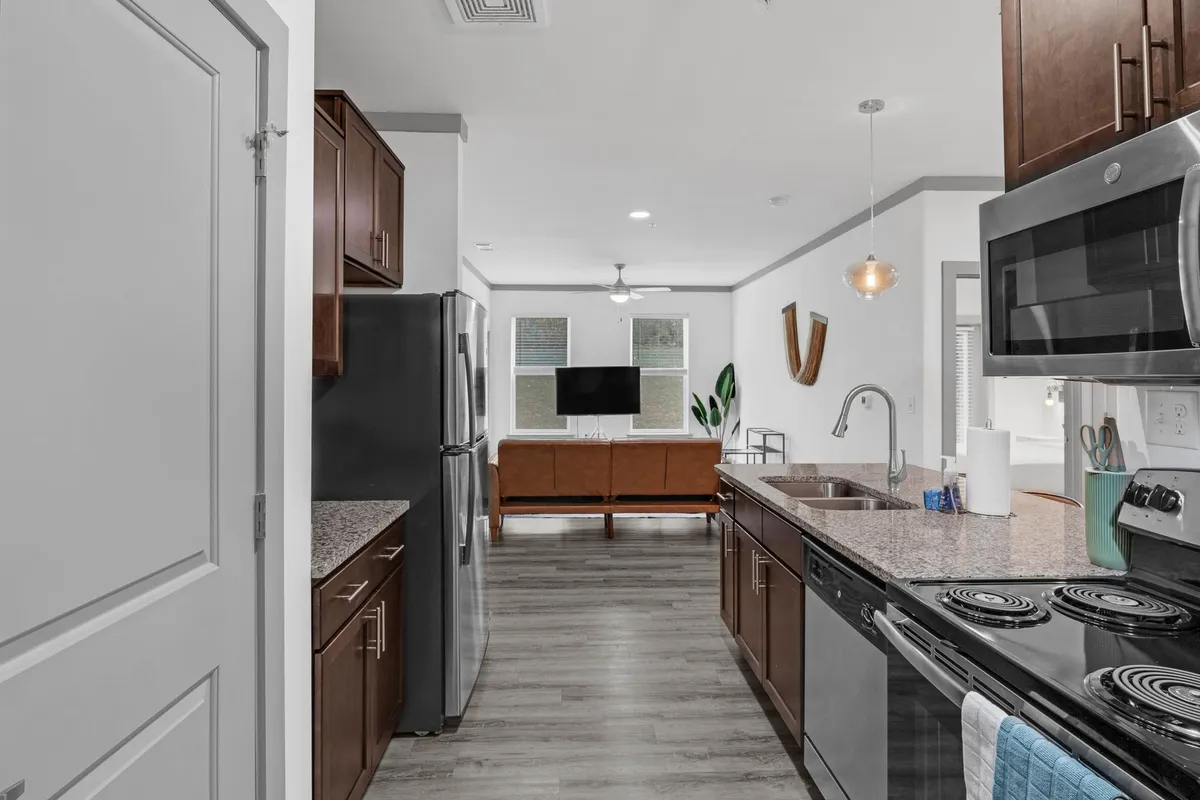 This image presents a spacious open-concept living area connecting the kitchen island, a comfortable seating area, and a television. The atmosphere is relaxed yet stylish, showcasing modern furnishings and a layout that promotes both entertaining and everyday living. Natural light and tasteful décor create an inviting space for arrivals and gatherings.