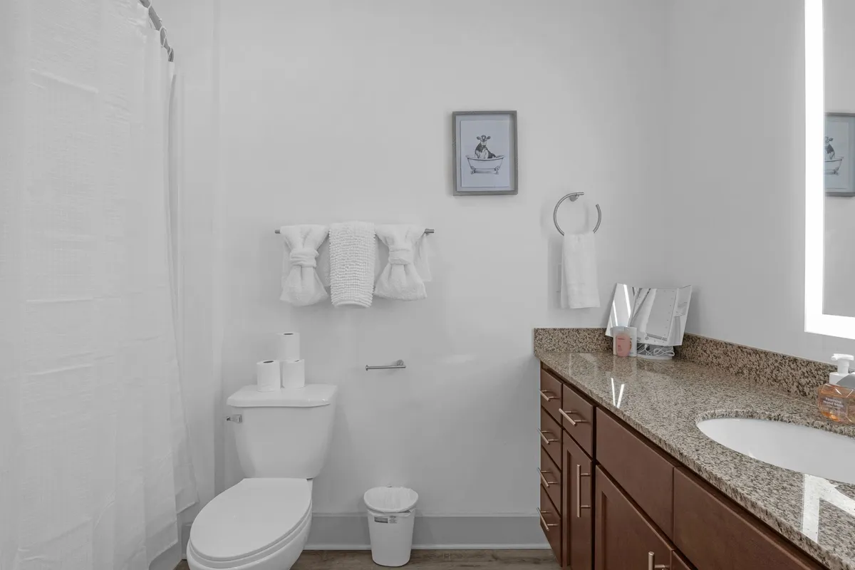 A modern bathroom featuring a granite countertop, framed artwork, and neatly arranged towels on a rack. The space is bright and calming, perfect for morning or evening routines. The design is clean and contemporary, supporting the idea of a move-in-ready home.