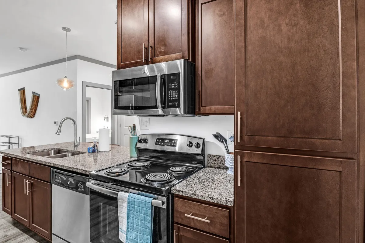 A modern kitchen featuring stainless steel appliances, a sleek granite countertop, and wooden cabinets. The space is designed for both meal preparation and casual socializing, offering a clean and organized environment.