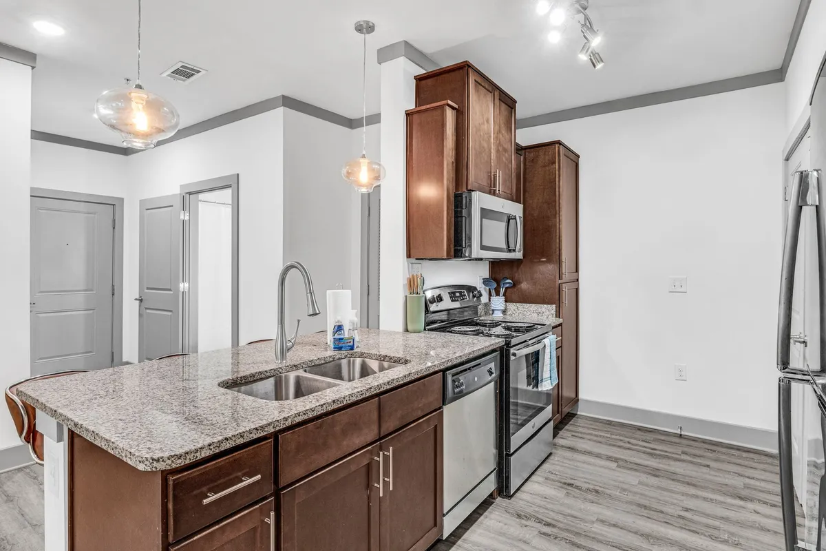 A stylish kitchen area with granite countertops, modern stainless steel appliances, and striking pendant lighting. The open layout is designed for both cooking and socializing, with a seamless transition to the dining area visible in the background.