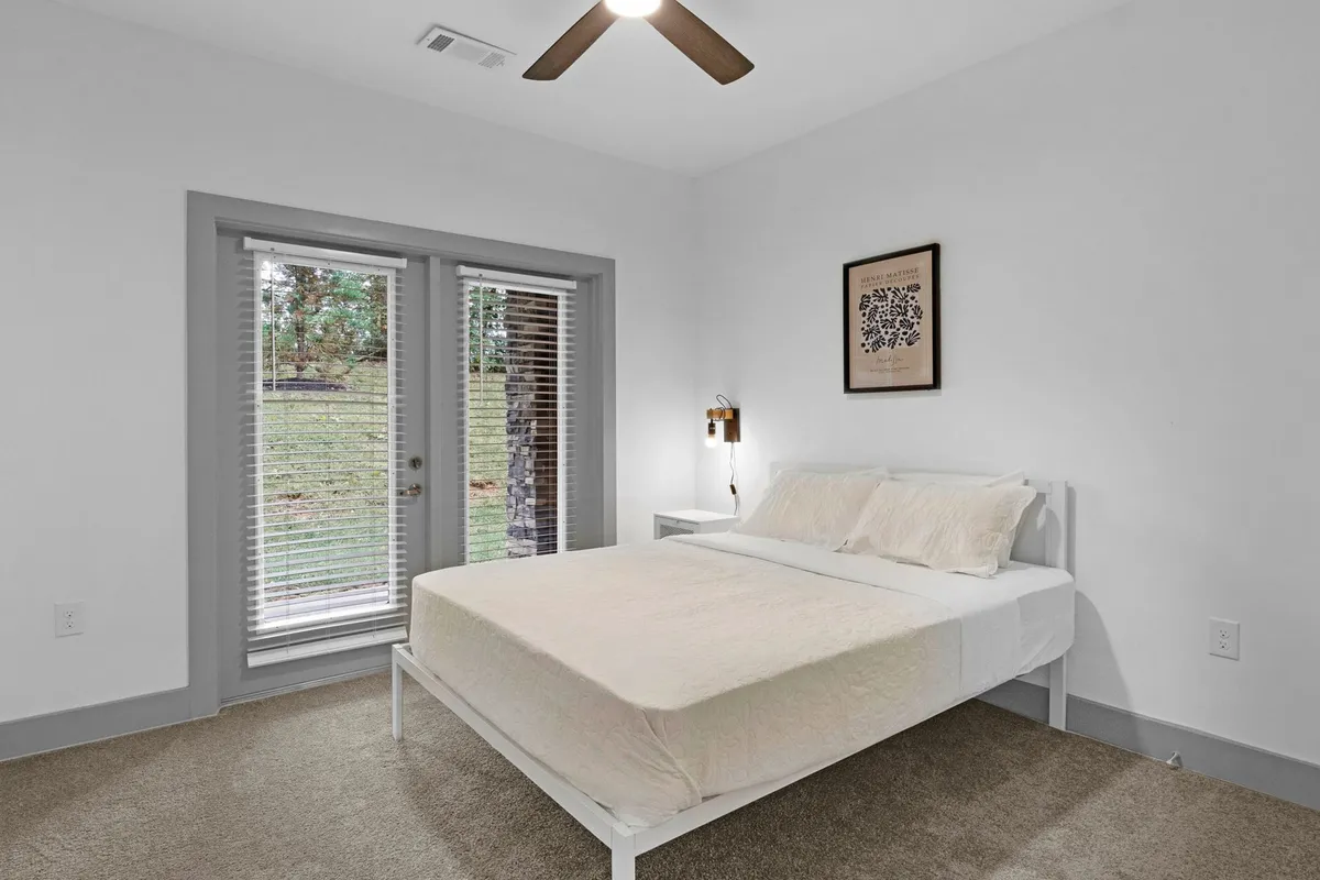 Another well-appointed bedroom with a comfortable bed placed against a backdrop of framed artwork, bathed in natural light from expansive windows and complemented by a cozy nightstand—ideal for reading and relaxing.