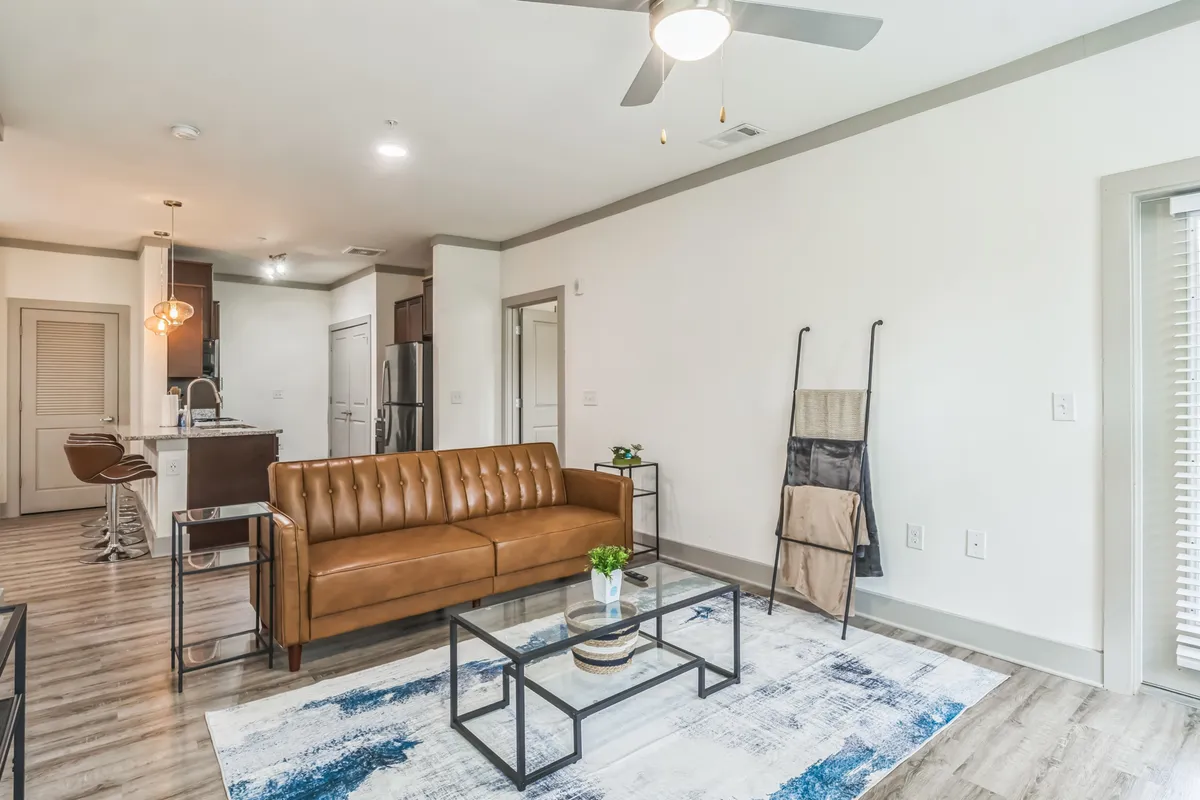 A cozy living room featuring a brown leather sofa, glass coffee table, and a decorative rug arranged to invite relaxation and conversation. The space is intimate yet airy, with thoughtful design elements that evoke a sense of comfort and style.